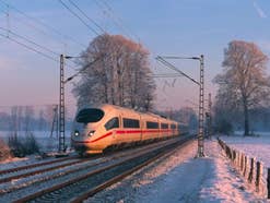 Ein ICE der Deutschen Bahn fährt durch eine Winterlandschaft. Die Gleise sind von Bäumen gesäumt, der Himmel ist blau-rosa gefärbt.
