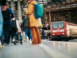 Zug fährt in ein Gleis ein, auf dem Leute stehen.