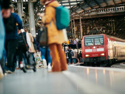Zug fährt in ein Gleis ein, auf dem Leute stehen.