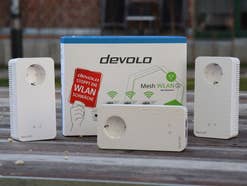 3 WLAN-Adapter stehen zusammen mit der Verpackung des devolo-Sets auf einem Holzuntergrund