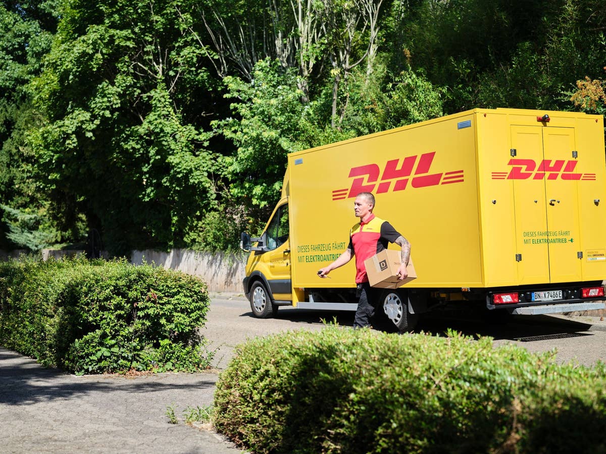 Ein DHL-Zusteller mit einem Paket unter dem Arm verlässt sein Lieferfahrzeug