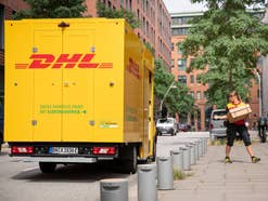 Eine DHL-Zustellerin neben ihrem Zustellfahrzeug