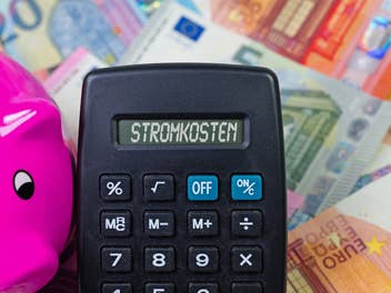 Stromkosten auf Taschenrechner mit Euroscheinen im Hintergrund und Sparschwein daneben