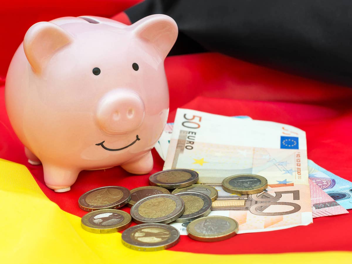 Sparschwein auf Deutschland-Flagge neben Geldmünzen und Euro-Scheinen.