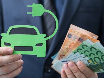 Mann hält ein Symbolbild für ein E-Auto und Euro-Geldnoten in der Hand.