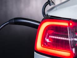 Linke Heckleuchte eines Tesla-Autos mit eingeschaltetem Licht, währen es an einem Ladekabel hängt.