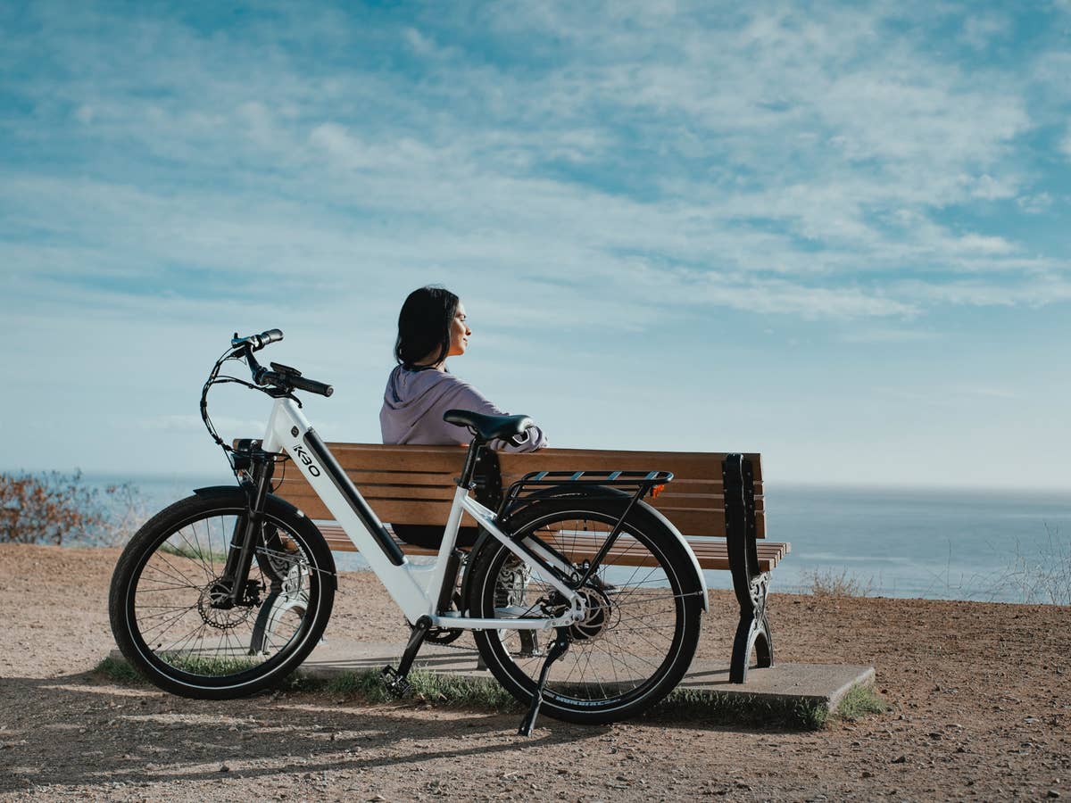 Eine Frau sitzt auf einer Bank, hinter ihr ein E-Bike