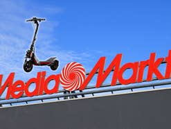 MediaMarkt-Logo vor einem blauen Himmel, daneben ein E-Scooter