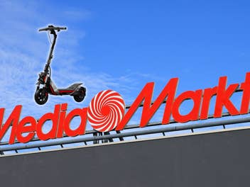 MediaMarkt-Logo vor einem blauen Himmel, daneben ein E-Scooter