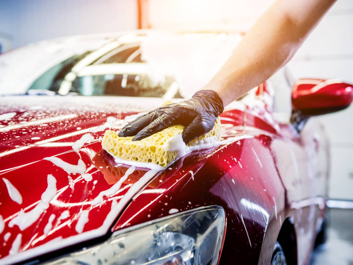 Mann wäscht die Motorhaube eines roten Autos mit einem Schwamm.