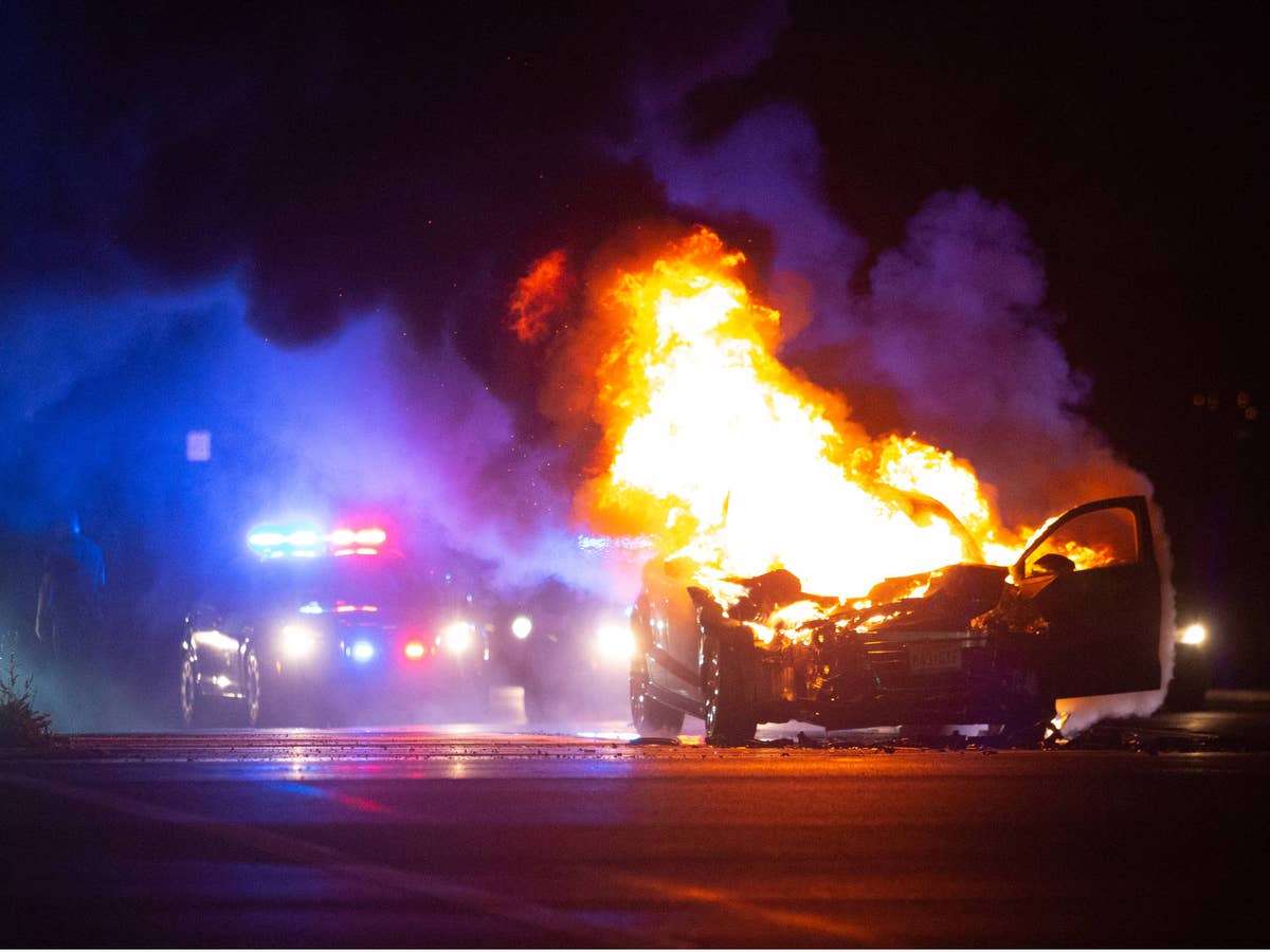 Auto brennt auf einem Highway bei Nacht mit Polizeiautos im Hintergrund.
