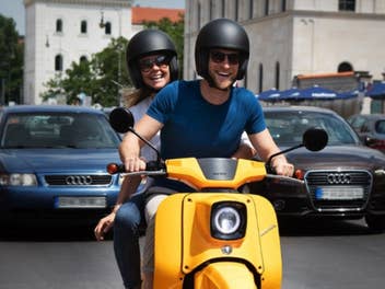 Personen sitzen auf einer eSchwalbe und fahren durch eine Stadt