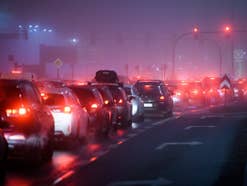 Viele Verbrenner in einer Schlange vor einer roten Ampel auf der Straße, bei Nacht.