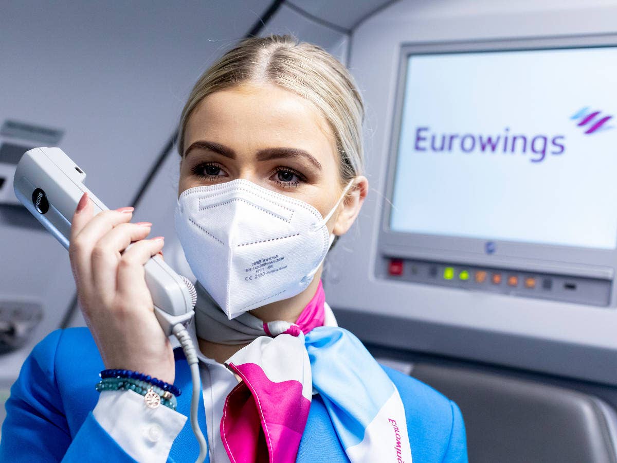 Flugbegleiterin von Eurowings macht eine Durchsage in der Kabine eines Flugzeugs.