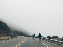 Drei Fahrradfahrer auf einer Straße, im Hintergrund Nebel.