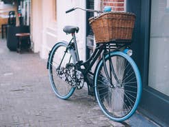 Ein Fahrrad mit blauen Reifen und braunem Körbchen steht an einer Wand.