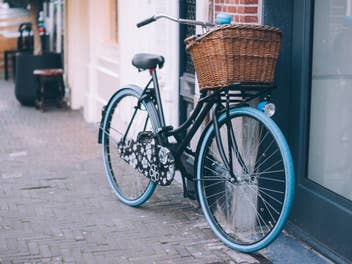 Ein Fahrrad mit blauen Reifen und braunem Körbchen steht an einer Wand.