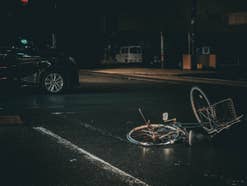 Ein Fahrrad liegt umgestürzt durch einen Unfall auf der Straße, im Hintergrund ein Auto.
