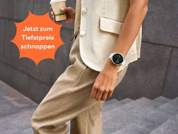 Ein Mensch, der eine Treppe heruntergeht, die Garmin Venu 4-Smartwatch am Handgelenk trägt und einen Kaffeebecher in der anderen Hand hat.