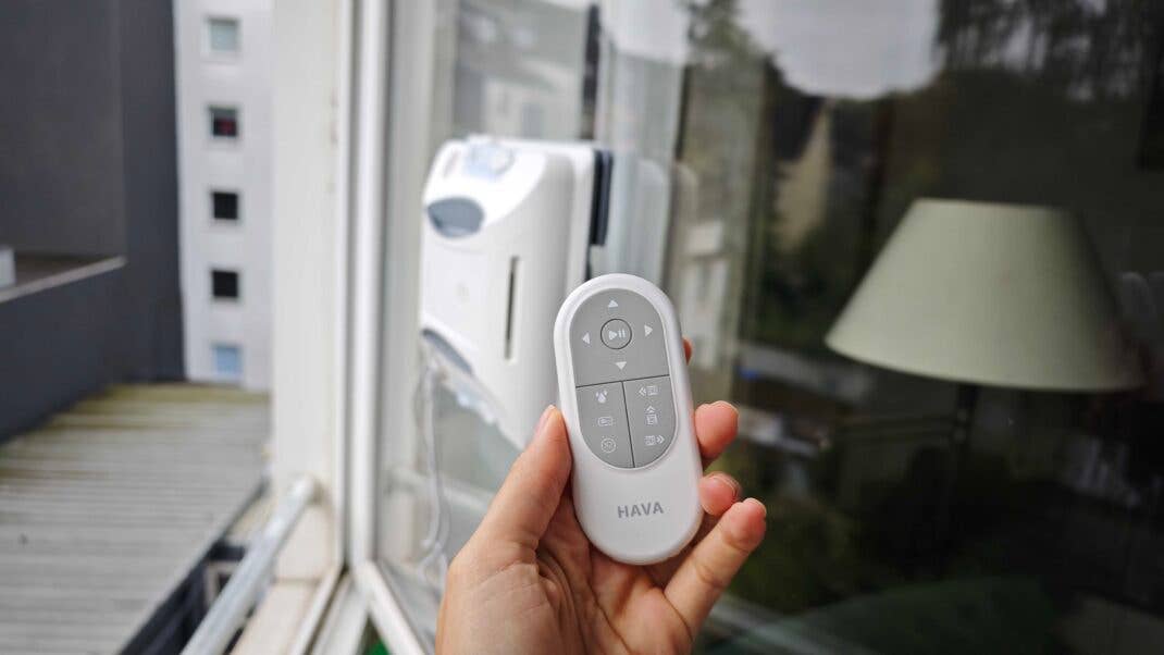HAVA U01 Fensterputzroboter im Hintergrund, Hand hält davor die Fernbedienung