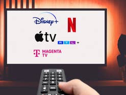 Fernbedienung auf einen TV gerichtet, auf dem die Logos von verschiedenen Streamingdiensten wie Netflix und Disney+ zu sehen sind