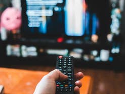 Eine Fernbedienung in einer Hand, die einen Fernseher im Hintergrund steuert