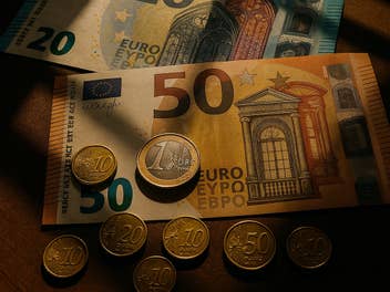 Euro-Geldmünzen und Euro-Banknoten im Sonnenlicht auf einem Schreibtisch als Symbolbild für eine Festgeld-Aktion der Hypovereinsbank.