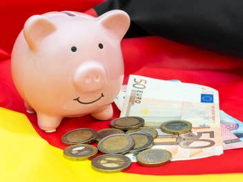 Sparschwein steht vor dem Hintergrund einer Deutschland-Flagge neben Münzen und Euro-Geldscheinen.