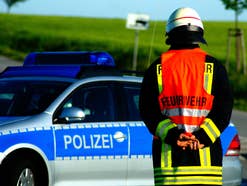 Eine Person der Feuerwehr vor einem Polizeiauto