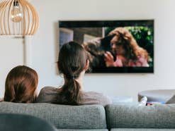 Zwei Frauen sitzen vor dem TV und schauen einen Film.