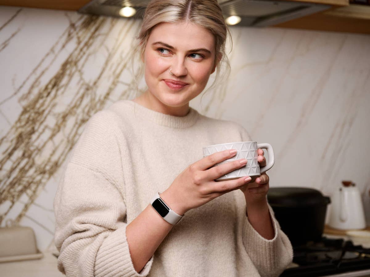 Fitbit Charge 6 am Handgelenk einer Frau mit Tasse in der Hand.
