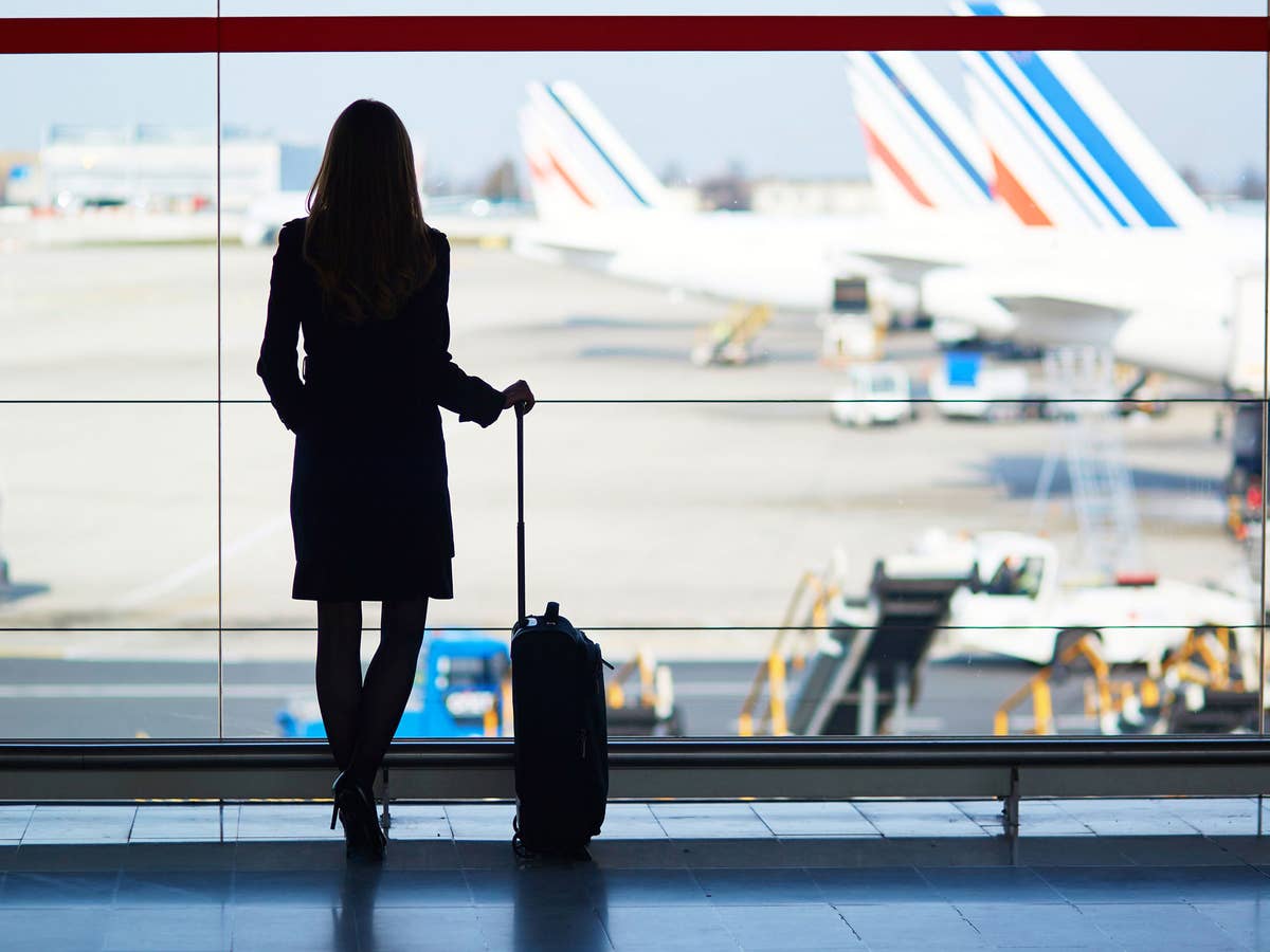 Eine Frau wartet mit einem Koffer am Flughafen