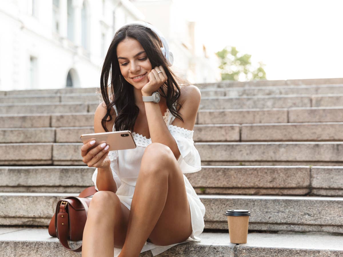 Eine Frau sitzt im Sommer auf einer Treppe und schaut auf ihr Smartphone