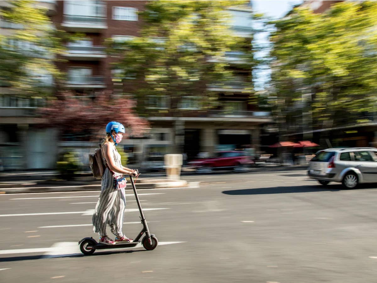 Frau fährt auf einer Straße mit einem E-Scooter.