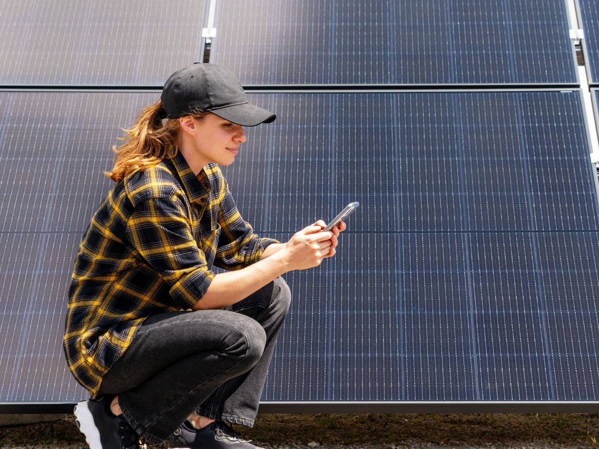 Beim Stromausfall bringt auch ein voller Akku nichts Eine Frau hockt vor einer Solaranlage mit einem Handy in der Hand