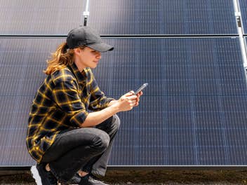 Eine Frau hockt vor einer Solaranlage mit einem Handy in der Hand
