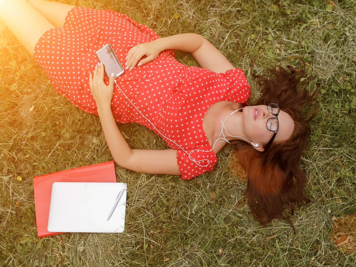 Eine Frau liegt im Gras und hört entspannt Musik mit dem Smartphone
