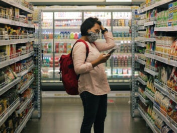 Frau mit Handy in der Hand vor einem Supermarktregal