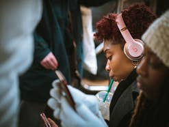 Eine Frau mit Kopfhörern trinkt aus einem Strohhalm Kaffee, streamt Musik und fährt U-Bahn