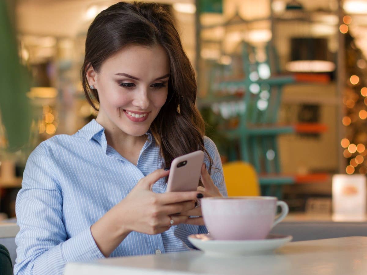 Frau mit Handy in der Hand und einem Kaffee