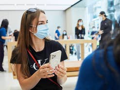 Frau mit iPhone in Apple Store Apple-Käuferin mit Maske