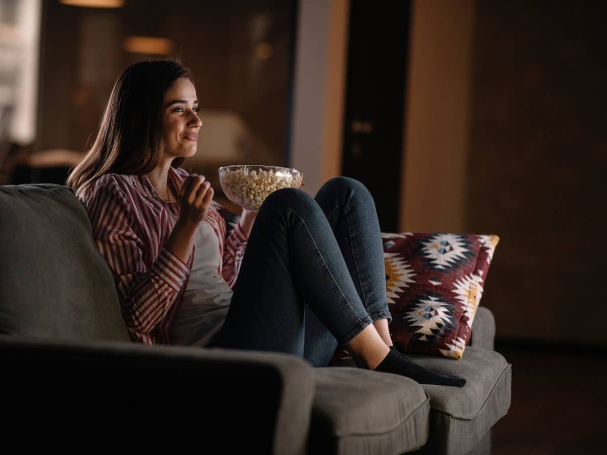 Frau streamt Serie oder Film, sitzt auf der Couch und isst Popcorn.