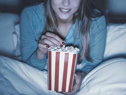 Eine Frau sitzt mit Popcorn im Bett und streamt eine Serie.