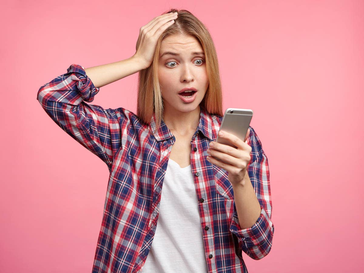 Frau mit Smartphone in der Hand legt verwundert Hand auf den Kopf.