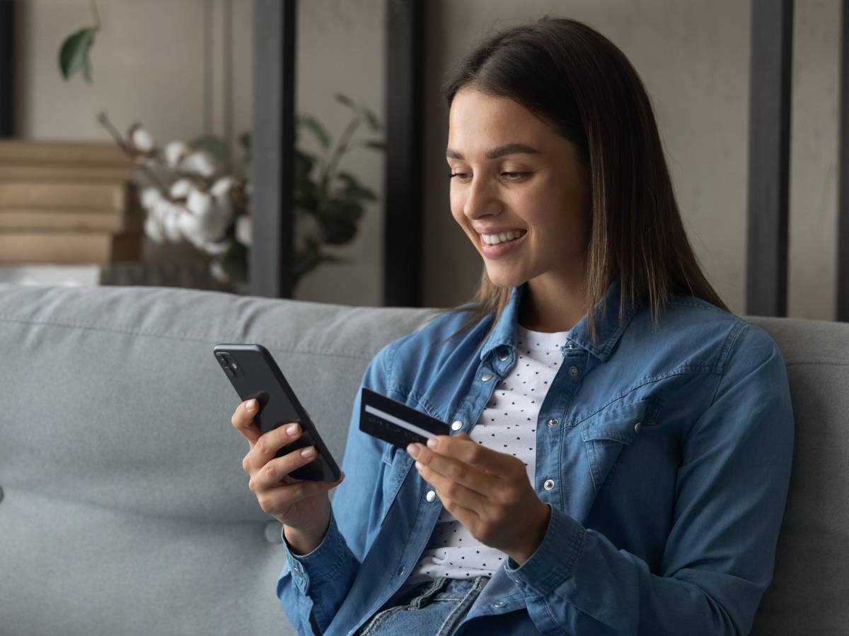 Frau sitzt auf einem Sofa und aktiviert auf einem Smartphone Prepaid-Guthaben.