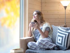 Frau mit Tasse Kaffee sitzend im Herbst zu Hause am Fenster