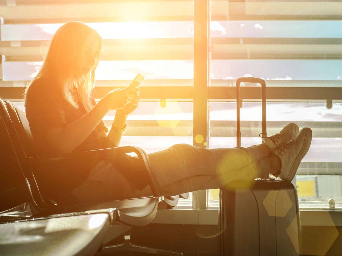 Eine Frau sitzt am Flughafen und schaut auf ihr Smartphone