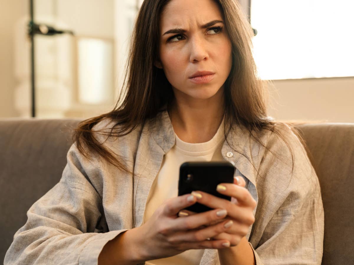 Frau mit Smartphone denkt über Unlimited-Tarif nach Frau sitzt auf der Couch mit ihrem Handy in der Hand und blickt kritisch