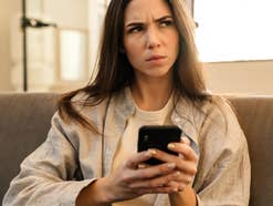 Frau sitzt auf der Couch mit ihrem Handy in der Hand und blickt kritisch