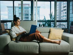 Eine Frau sitzt mit einem Laptop auf dem Sofa und streamt einen Film.